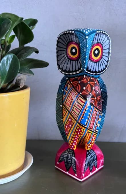 Hand-carved, hand-painted wooden owl beside a potted plant